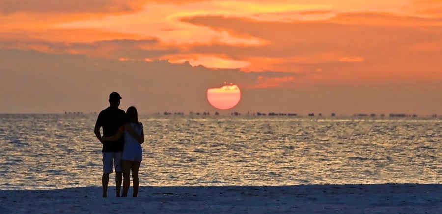 A couple with arms to each other enjoys watching the sunset on Sanibel Island.