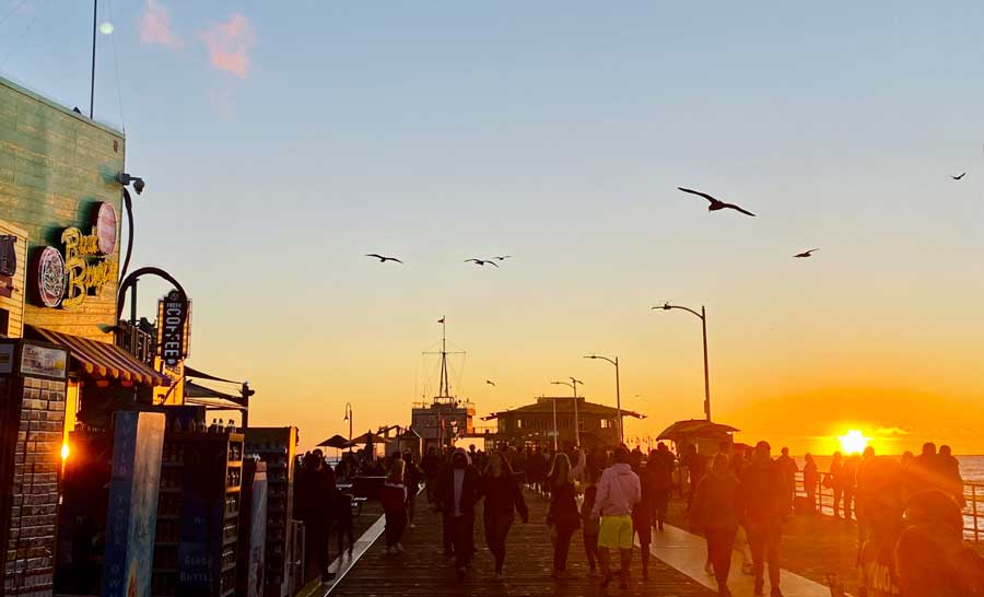 View of people in Santa Monica Pier and birds flying over it during sunset