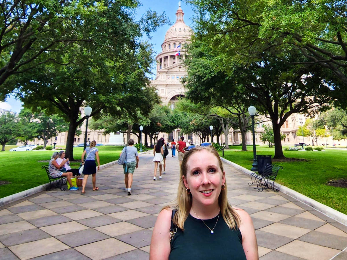 The author Sarah Heath, posing for a photo at the park with the Texas State Capitol in Austin