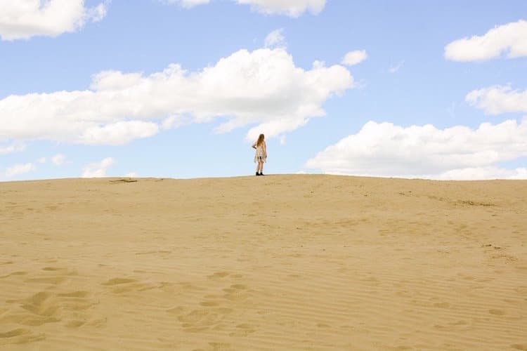 Taylor stands on a hill at the Great Sandhills of Saskatcehwan with a blue cloudy sky behind.