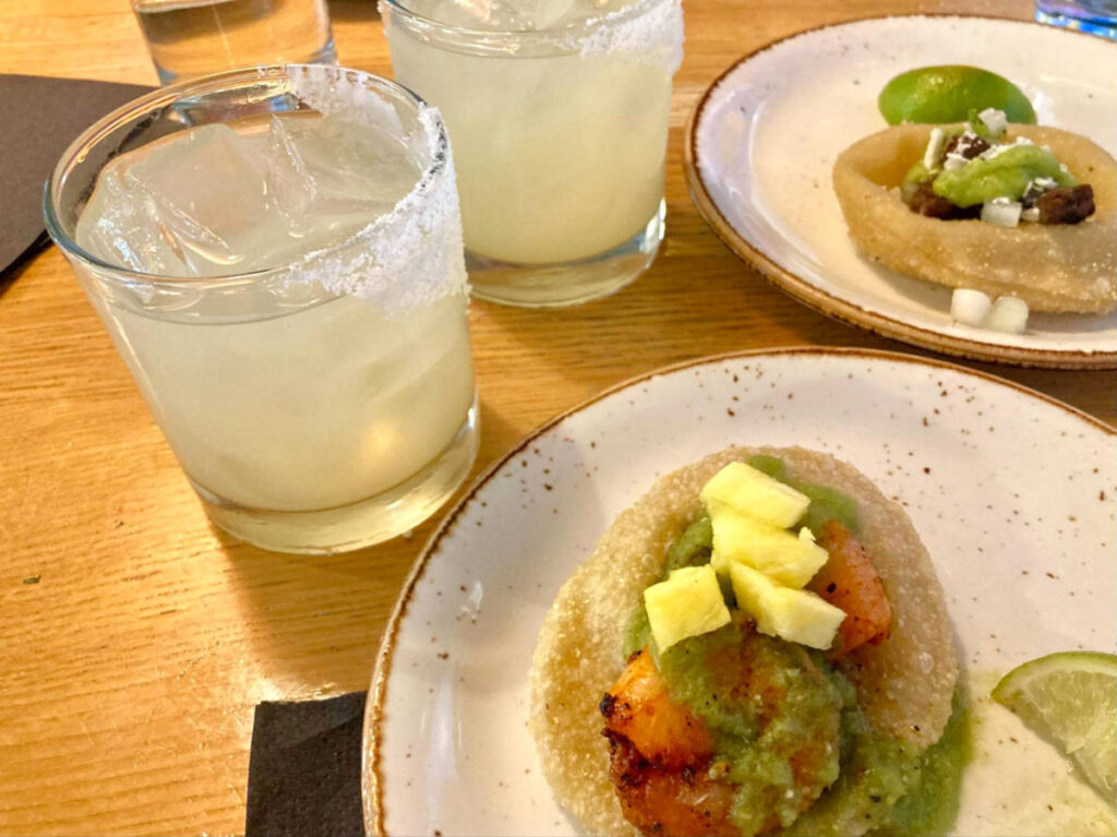 Two plates with savor fry bread tacos and glasses of cocktails