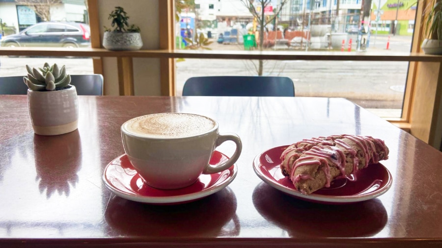 A cup of oat milk latte and lavender lemon scone on the table with the Pearl District view from the window of the restaurant