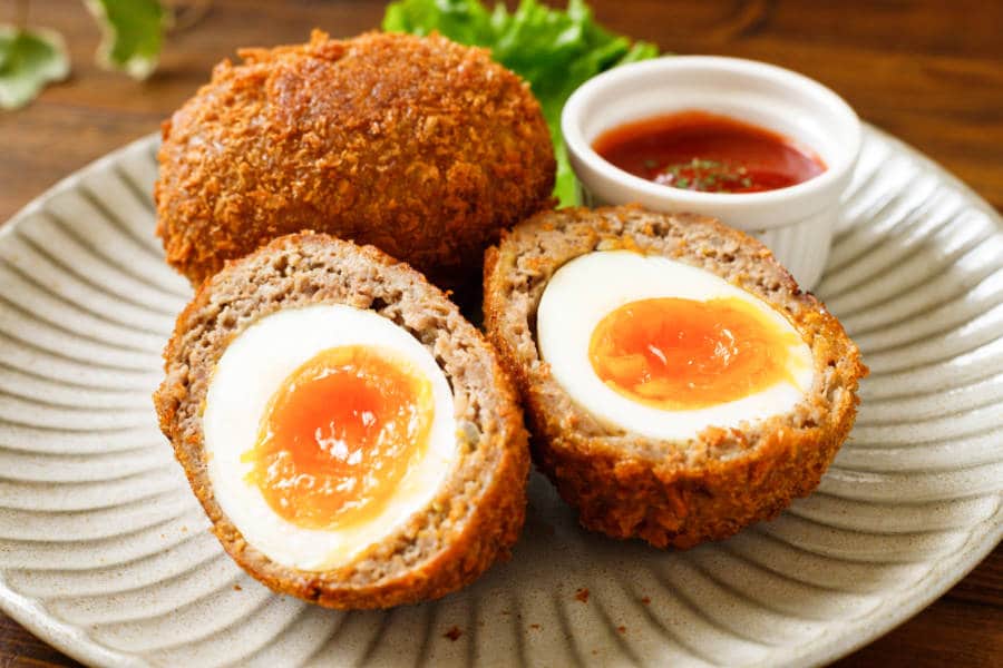 A plate of Scotch eggs with dipping sauce on the side