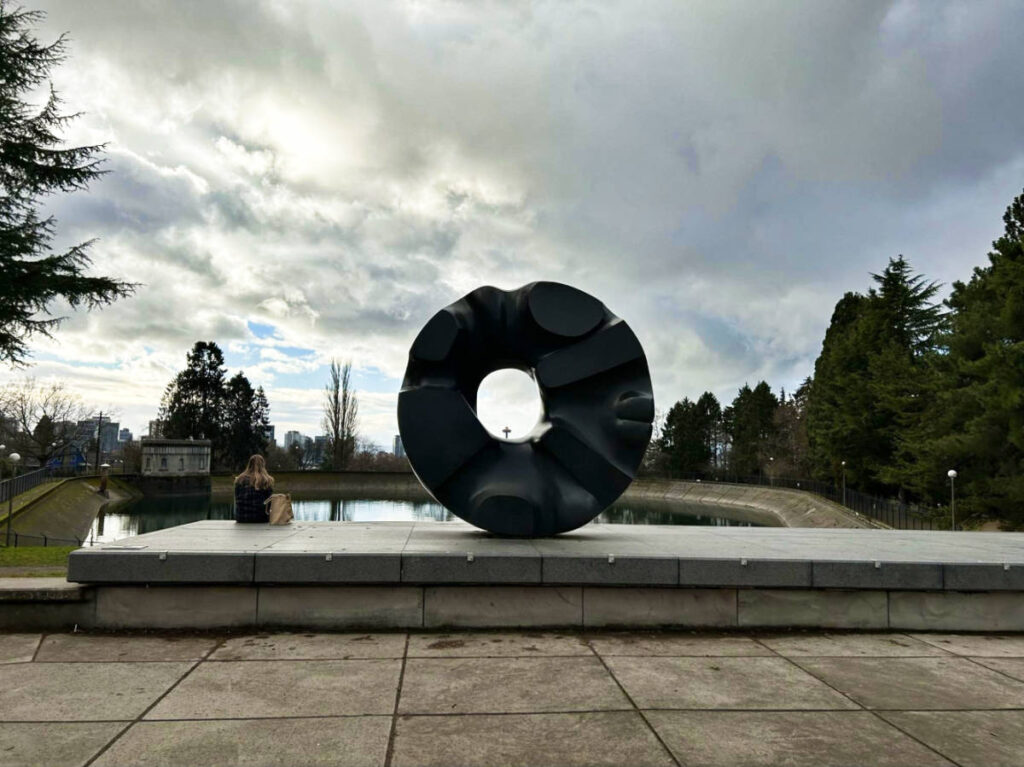 The Black Sun sculpture framing the Space Needle from a distance on a gloomy day