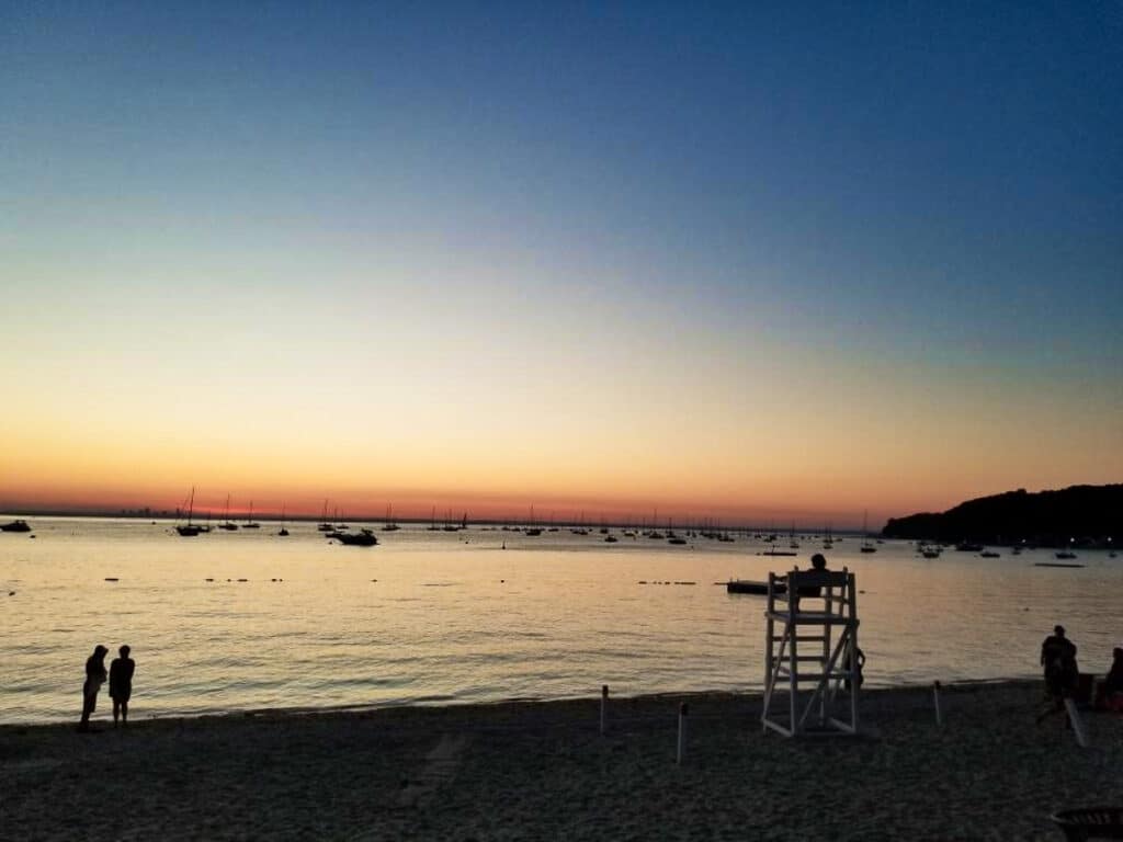 View of the silhouette of people at the shoreline of Sea Cliff Beach during sunset