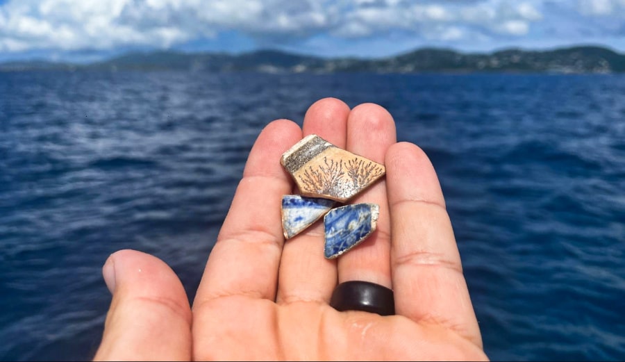 A hand with fragments of centuries-old porcelain near the ocean in St. Thomas