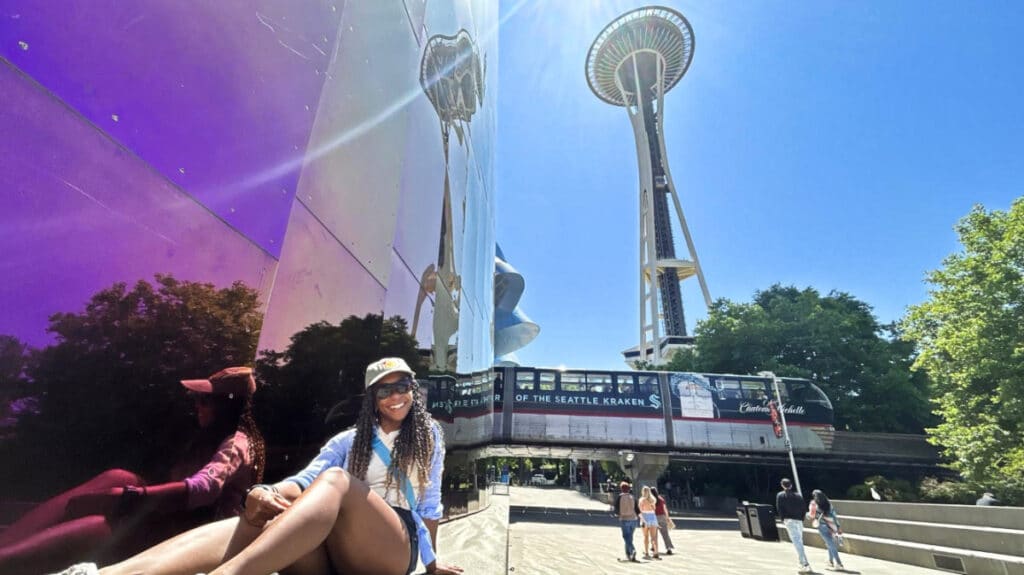 The author Chelsea Booker, posing in the Museum of Pop Culture with the Monorail and Space Needle in the background at Seattle Center