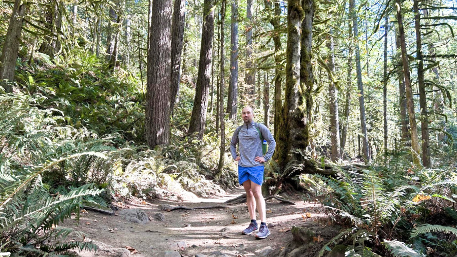 A man posing on a hiking trail in the middle of the forest.