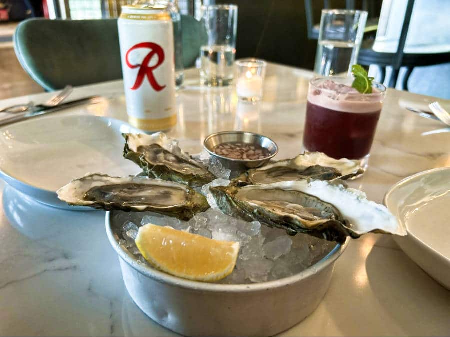 Oysters with a slice of lemon on the top of the ice and different drinks on the side