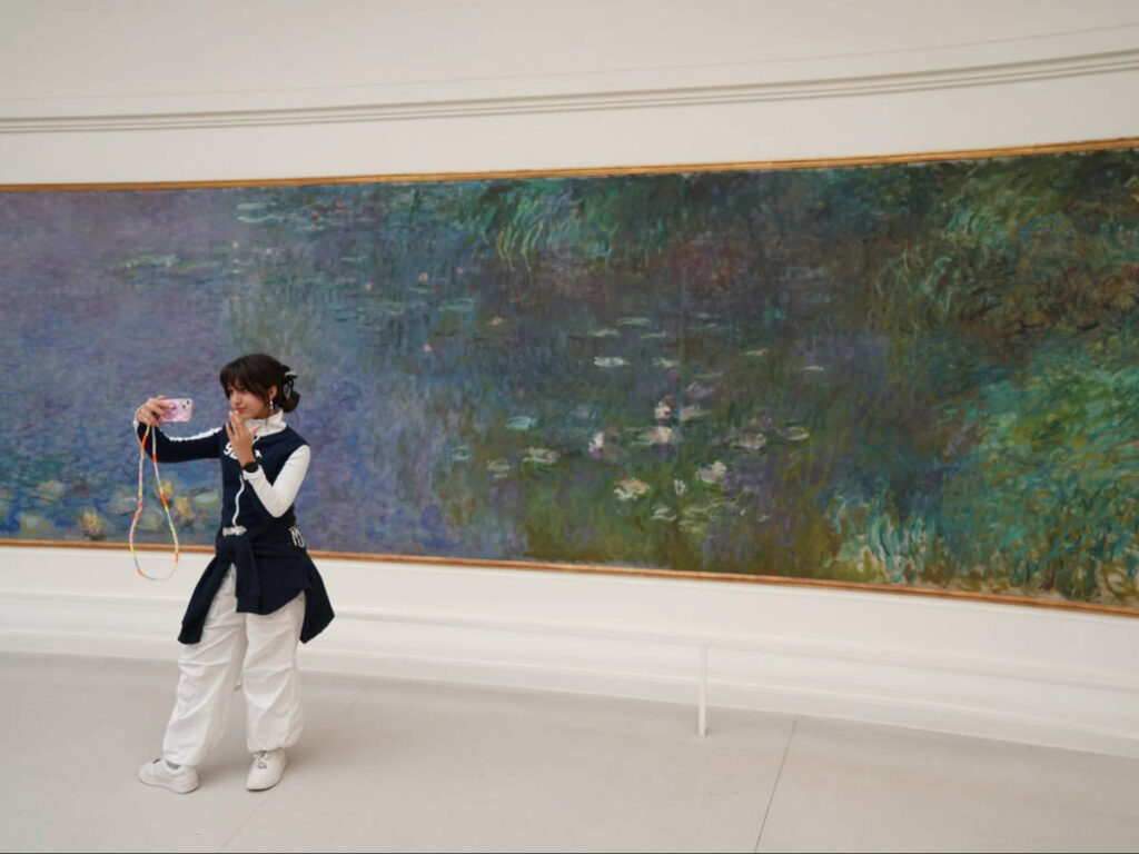 A woman taking a photo in front of the Monet’s Water Lilies Mural