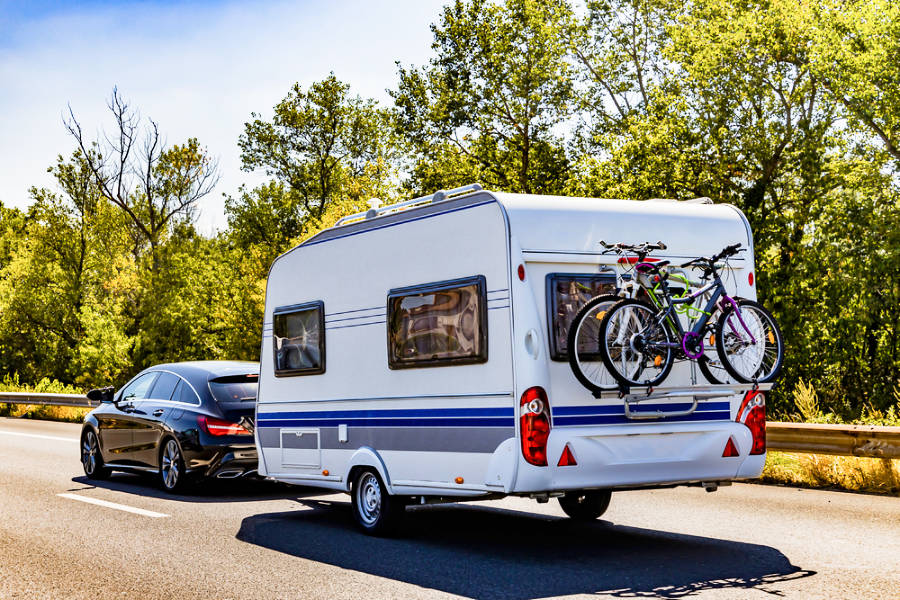 A sedan with a caravan trailer with bicycles on the racks at the back