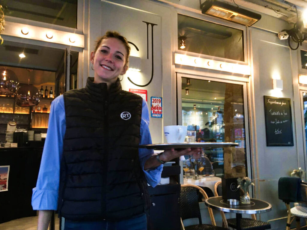 Iris, the server at a Marais restaurant posing for a photo while holding a serving tray