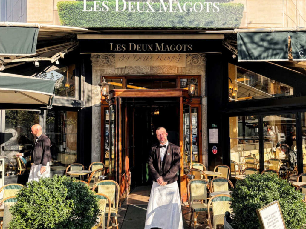 The server posing at the entrance of Les Deux Magots Café