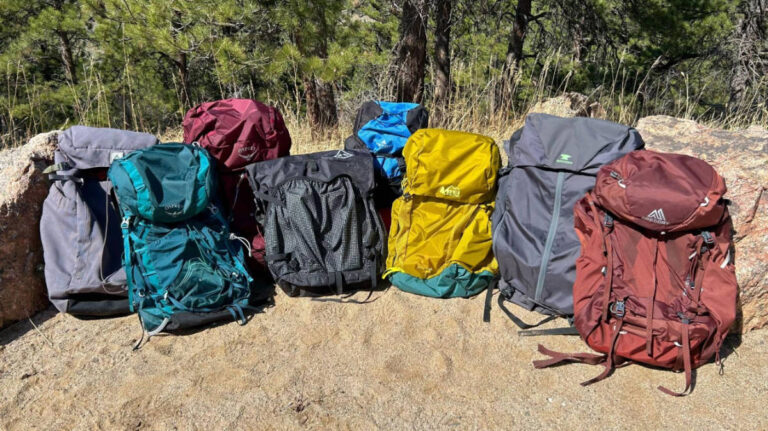 A row of colorful backpacks arranged neatly on a large rock
