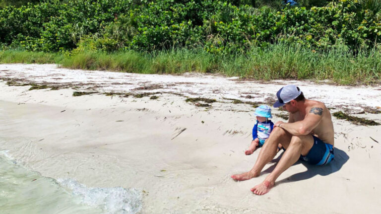 A man and a child sitting at the shoreline of South Lido Beach