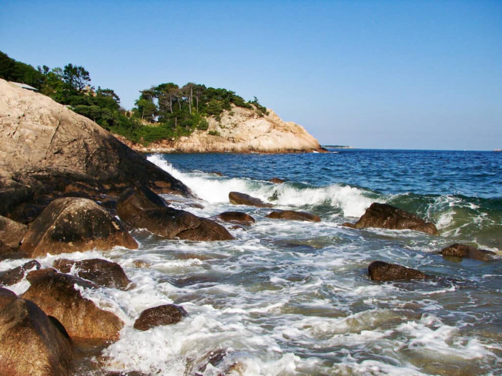 View of the clear blue water surrounded by rocky shoreline and mountain views in Singing Beach
