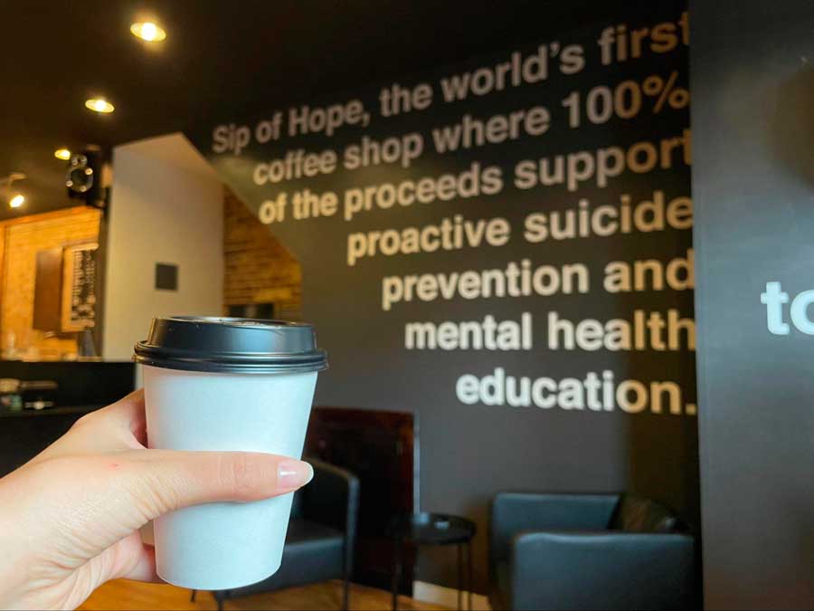 The author holding her cup of latte with a background from Sip of Hope