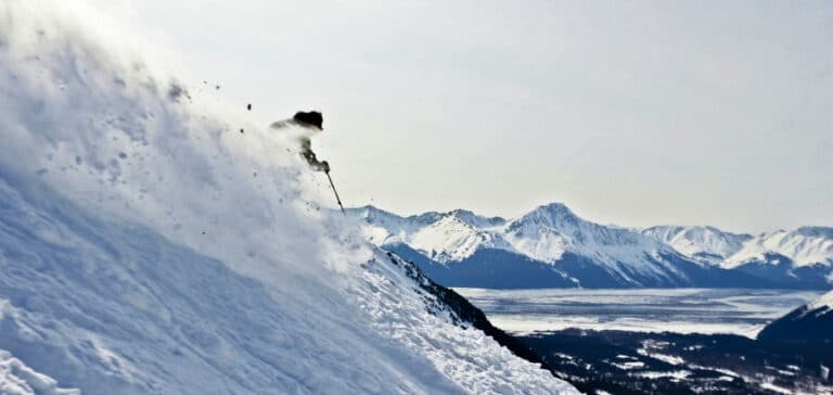 A skier going down the slope in Alaska with a scenic view in the background