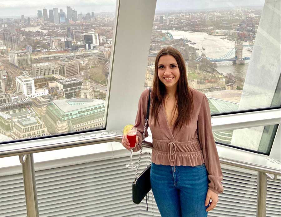 The author holding a cocktail in Sky Garden with a view of the Tower Bridge on her background
