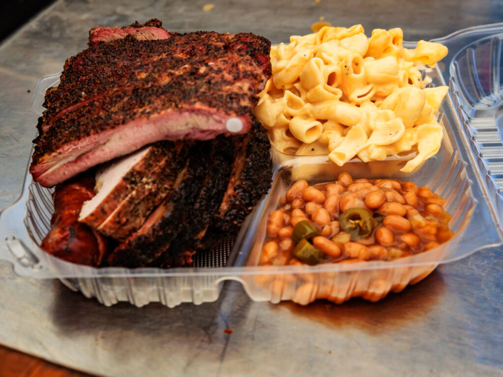 A plate of barbequed meats with sides of beans and macaroni and cheese
