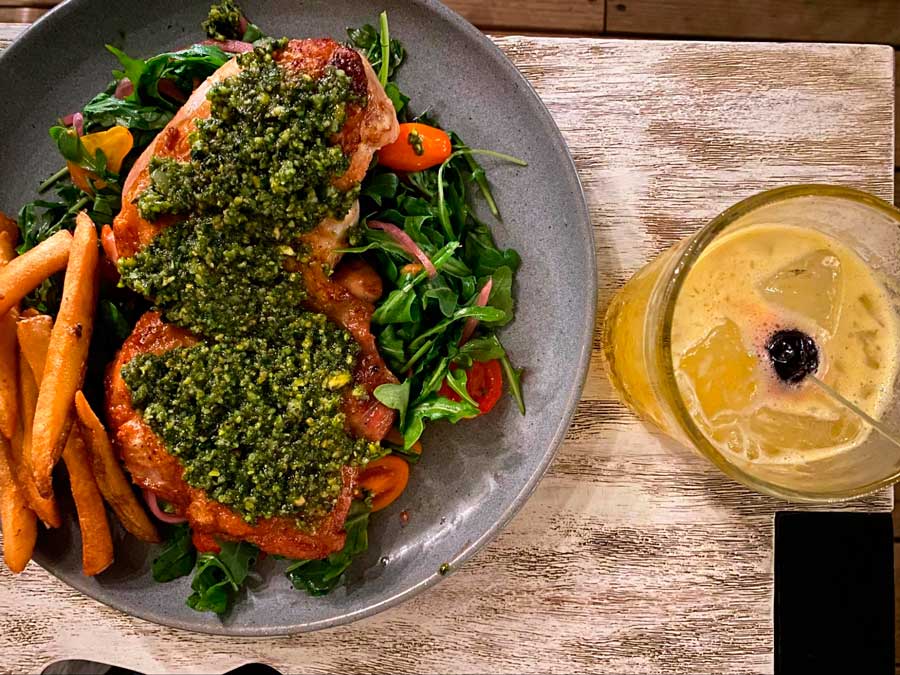 A pistachio basil pesto chicken on a plate and a glass of cocktail