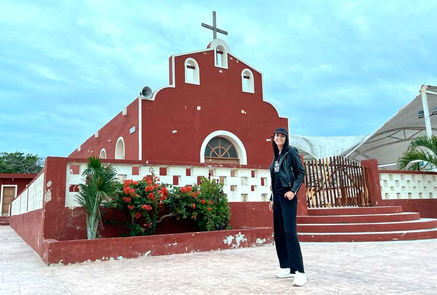 View of Clara in front of a small red church in El Cuyo