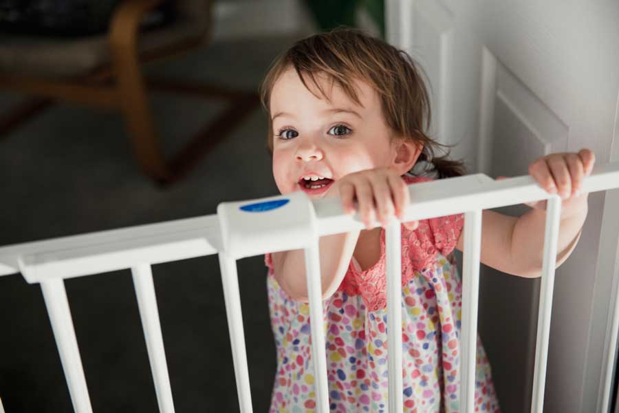 A little girl standing while holding on a baby gate