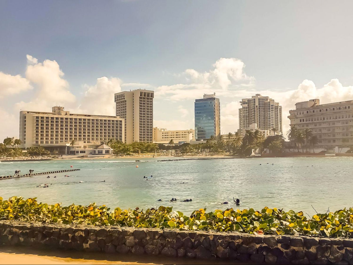 A scenic beach with people snorkeling and buildings in the background in La Pecera