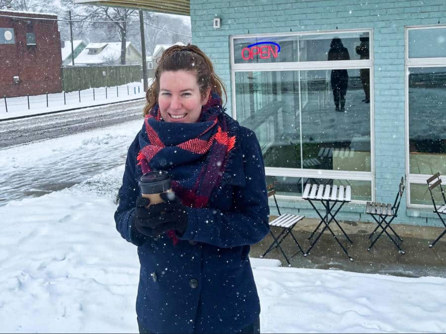 The author Elizabeth Demolat standing outside in the snowy weather while holding a coffee cup