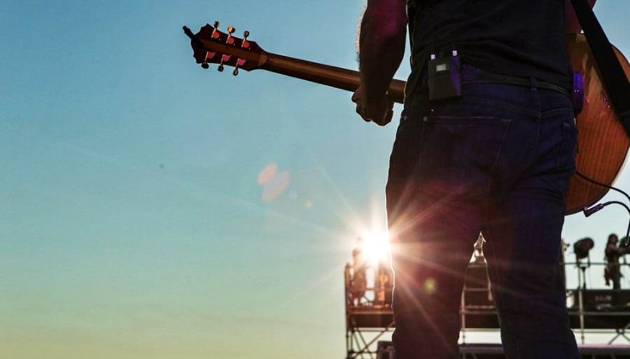 A man playing guitar on stage under stage lights.