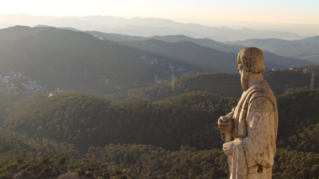 A statue overlooking the scenic view of the mountains of Collserola Park