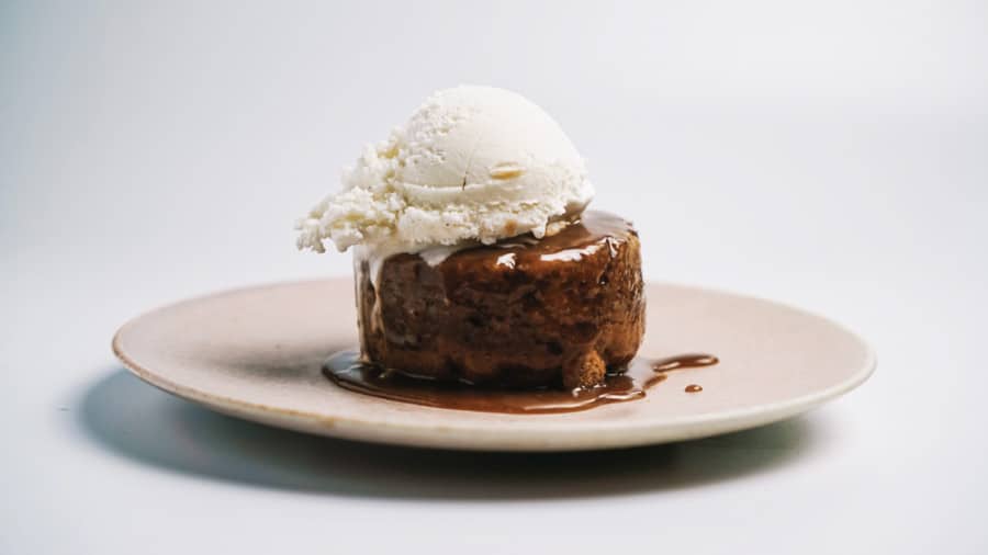 A plate of sticky pudding topped with vanilla ice cream and sauce