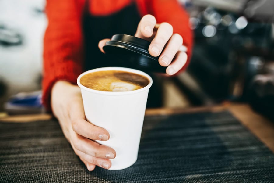 View of a barista's hands serving a paper cup filled with coffee