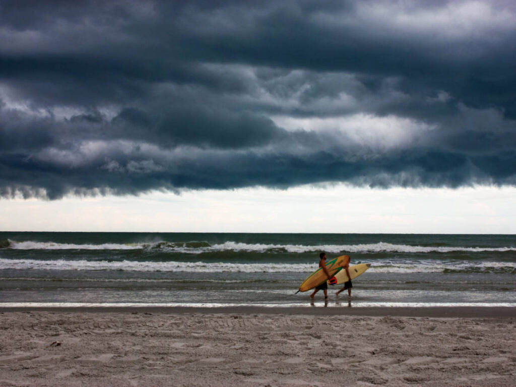 View of surfers walking along the shoreline with the dark clouds above the beach in Jacksonville