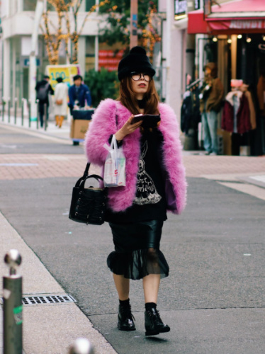 A woman in pink fur coat and black hat strolling down the street on a chilly day