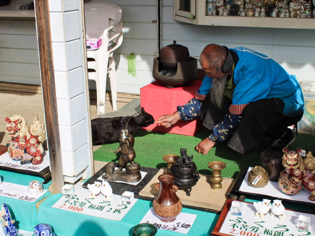 A man feeding the cat at Oshino Hakkai with displayed products around