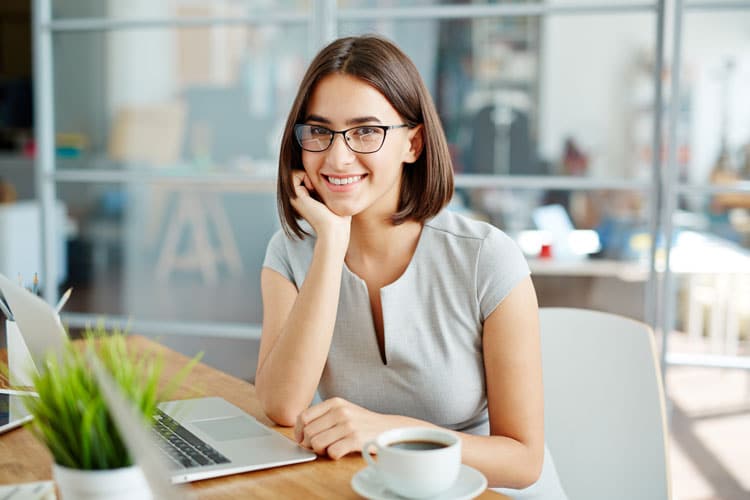 smiling woman sitting with laptop and cup of coffee
