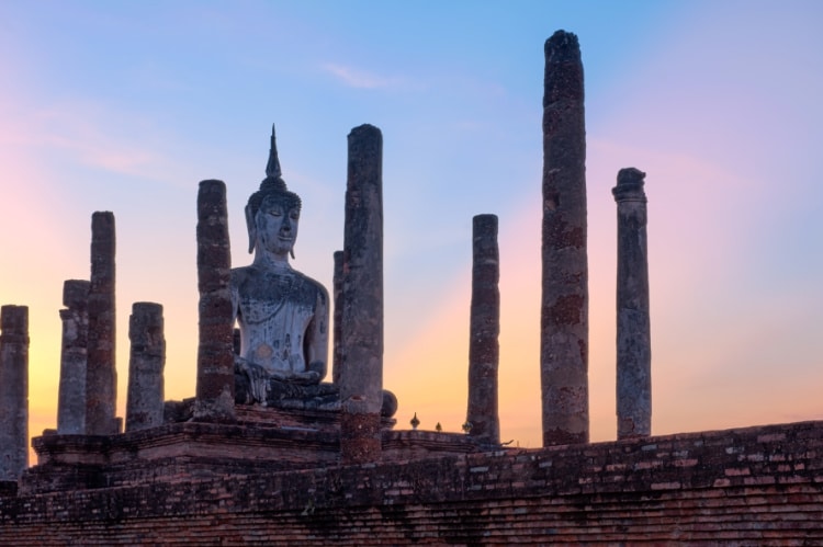 Majestic view of Buddha statue surrounded by columns with the warm glow of the setting sun in the background
