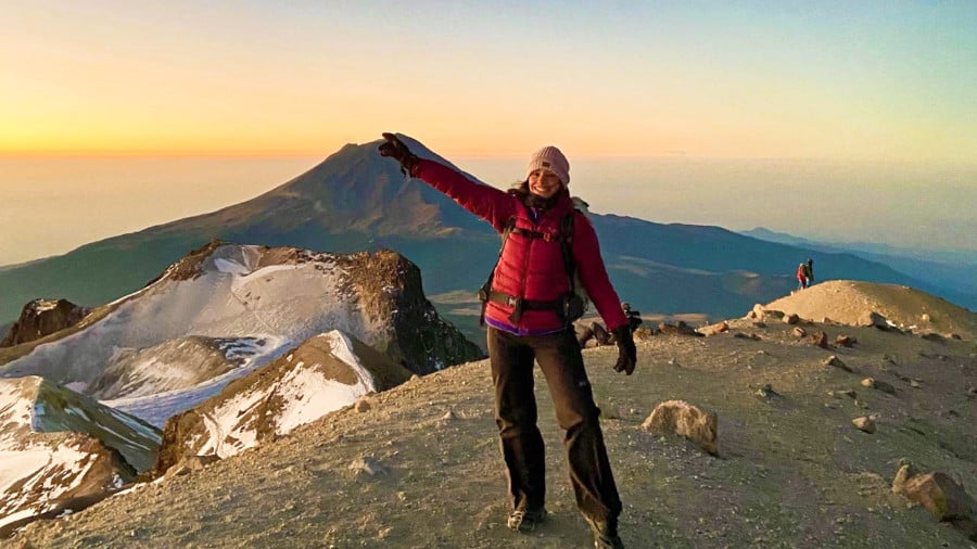 The author McKenna Mobley posing at the summit of Iztaccihuatl with the famous Popocatepetl Volcano in the background during sunset