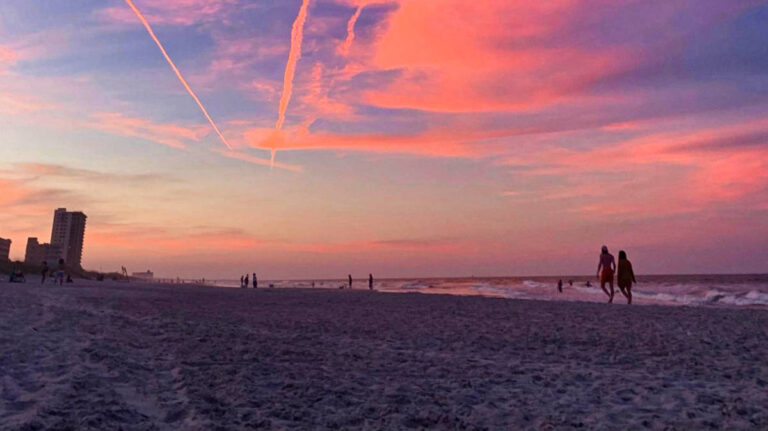 A couple walking on the sandy beach with skyline views at sunset