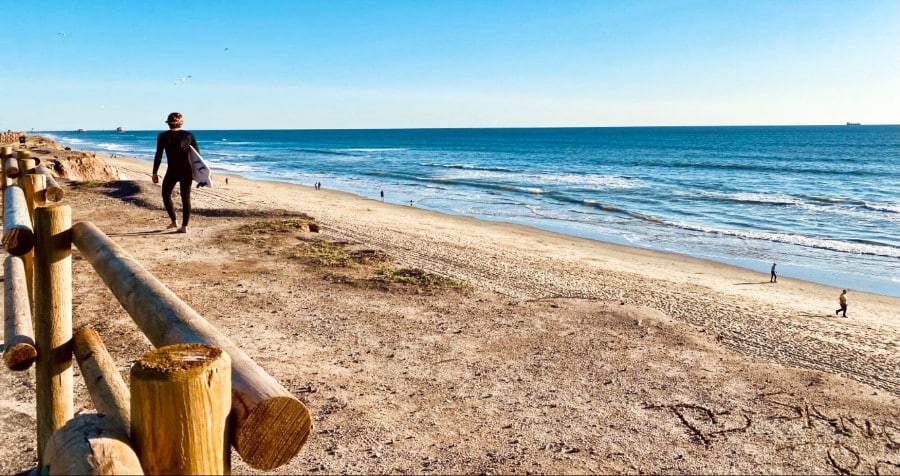 A surfer walking along the beachfront on a sunny day
