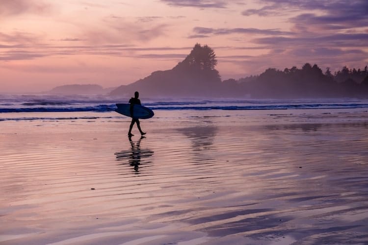 A person goes surfing in Tofino, Vancouver Island with a pink and purple sky