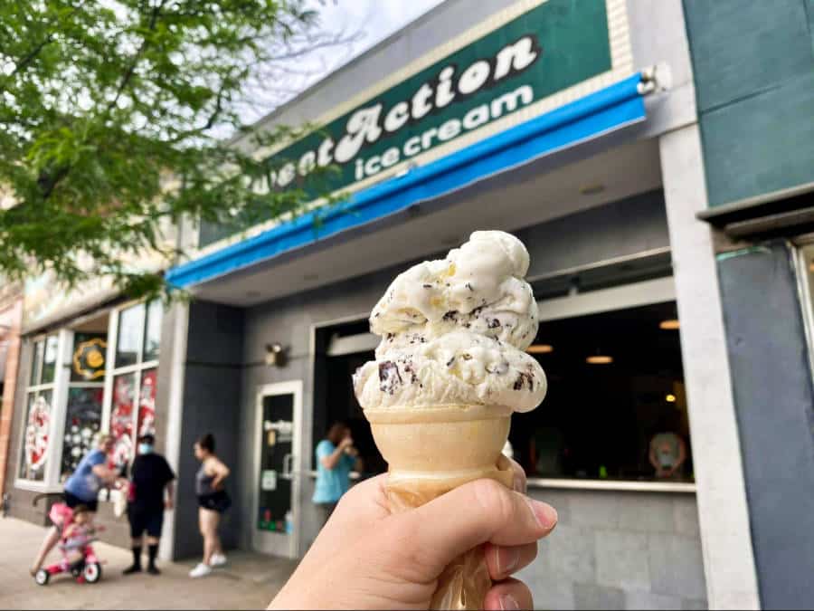 A hand holding an ice cream in a cone outside Sweet Action