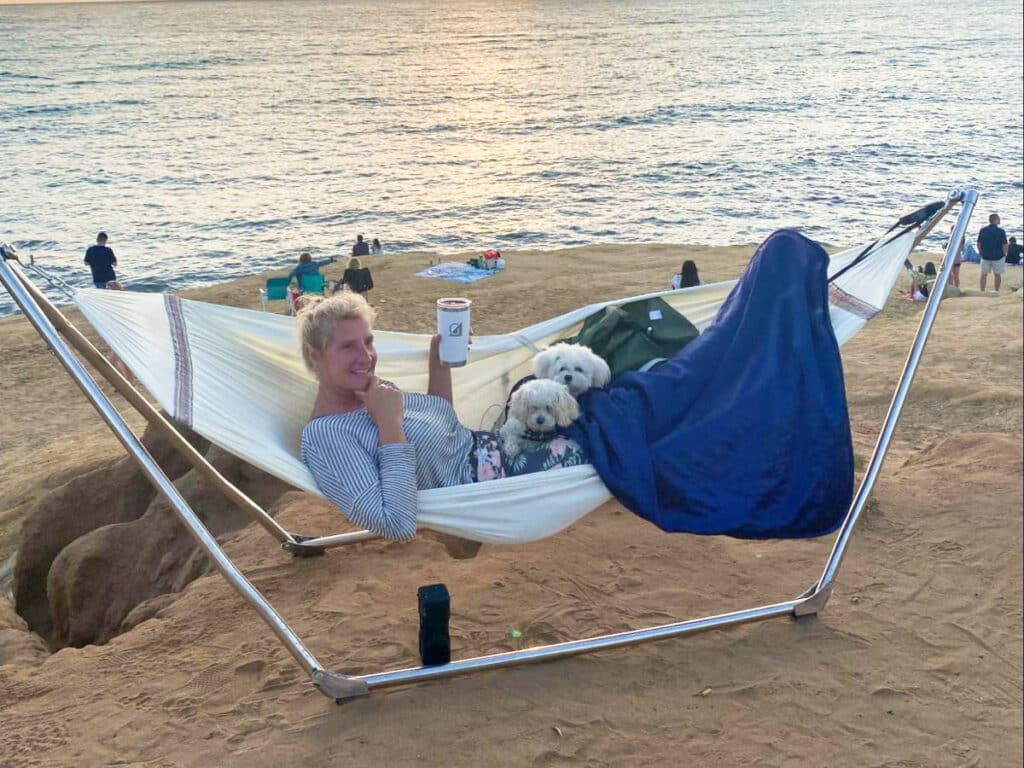 A woman with her dogs on a hammock near the beach at sunset