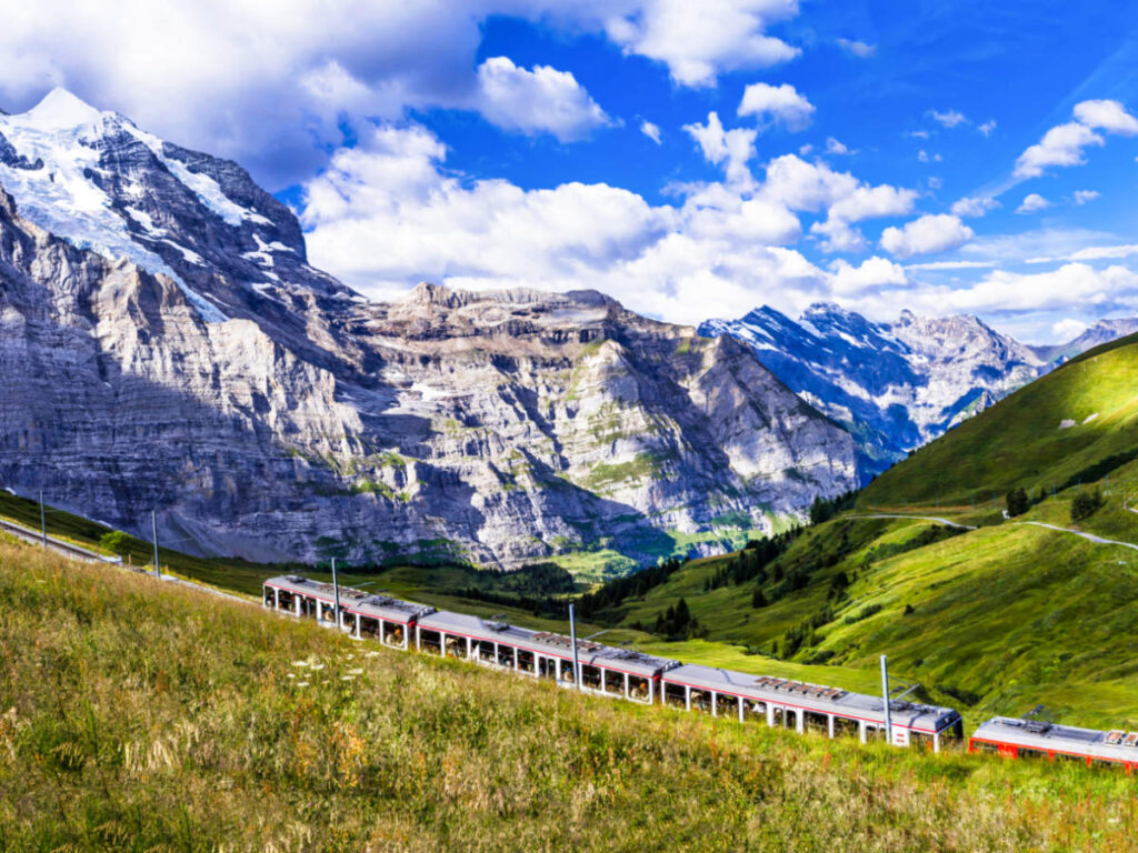Picturesque view of the train, green landscape and snow capped Alps mountains