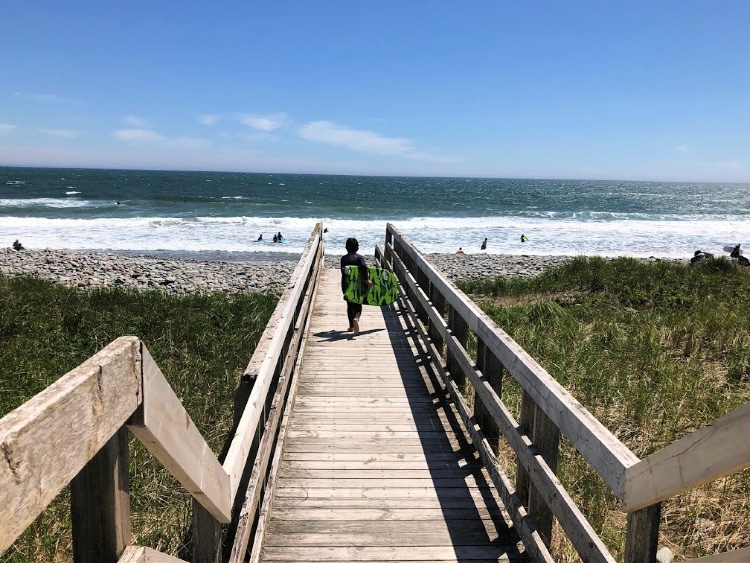 Young surfer carrying a body board under his arm, walking along a boardwalk to Lawrencetown beach
