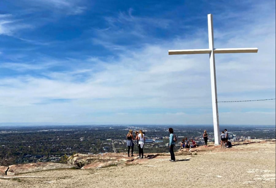 People enjoying the scenic view near a big cross from the top of the Table Rock trail
