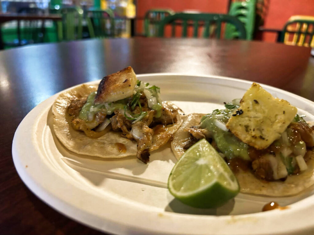 A plate with two tacos and sliced lime from Tacos Chukis