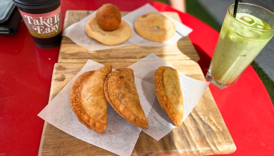 A glass of iced matcha latte with pandebono and a variety of savory empanadas served outside the Take it Easy bakery in Vegas