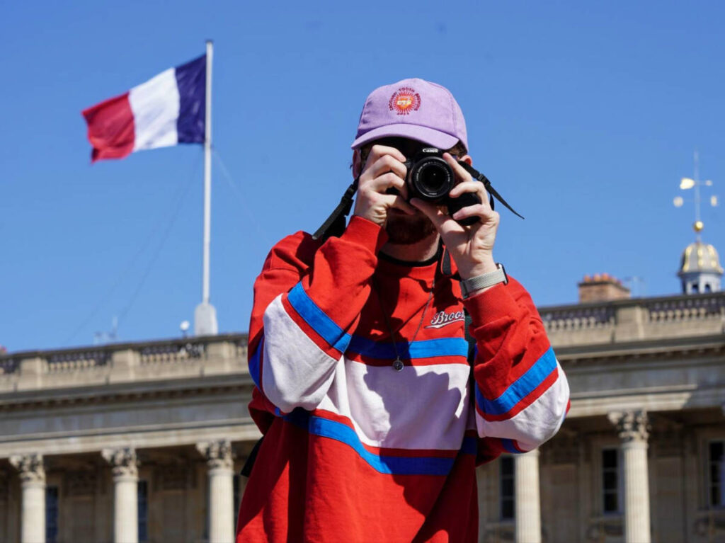 A man taking photos with the France flag in the background